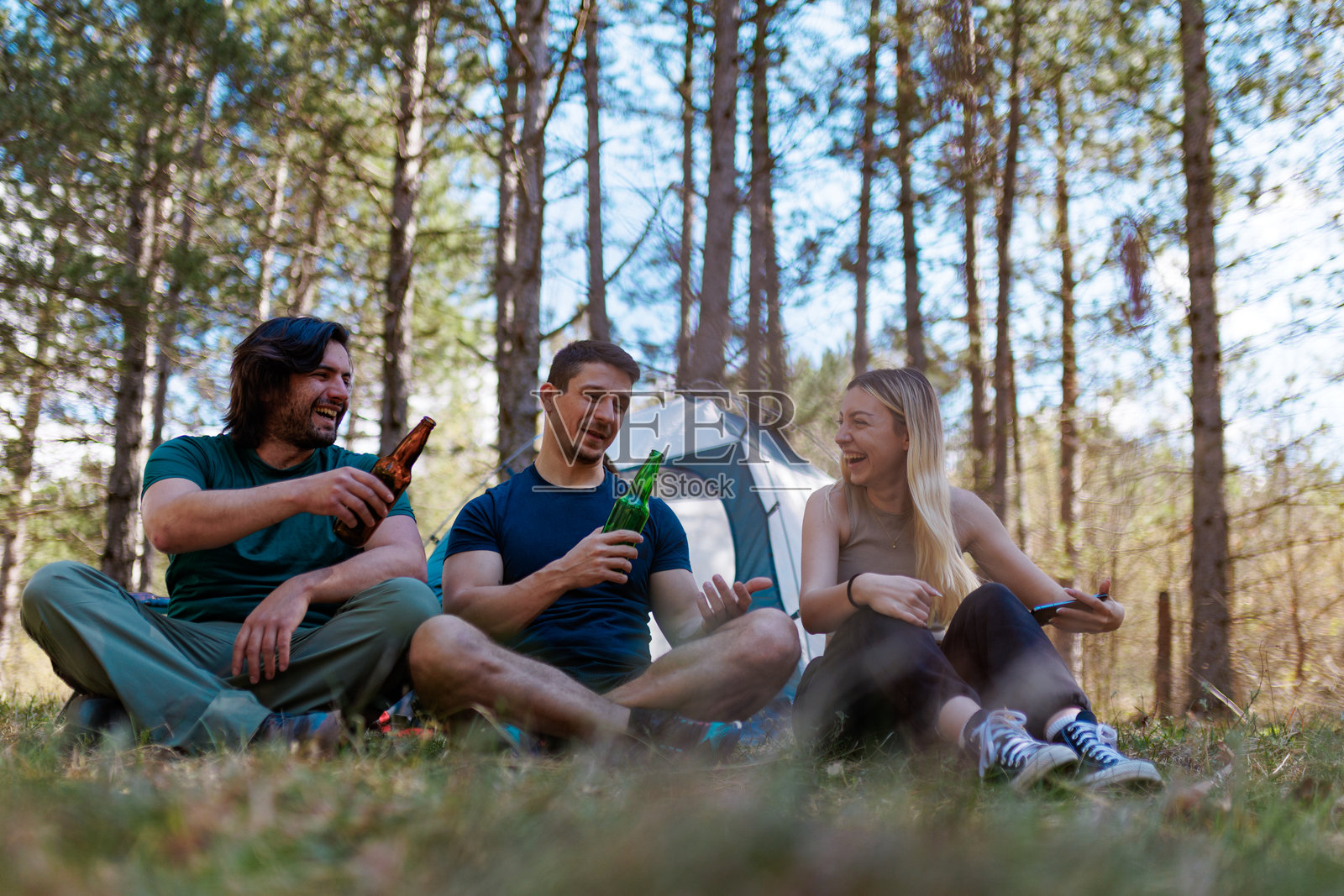 朋友们在阳光明媚的夏日,在树林中享受悠闲的露营时光,一边分享饮品,一边开怀大笑,周围是美丽的自然风光。照片摄影图片