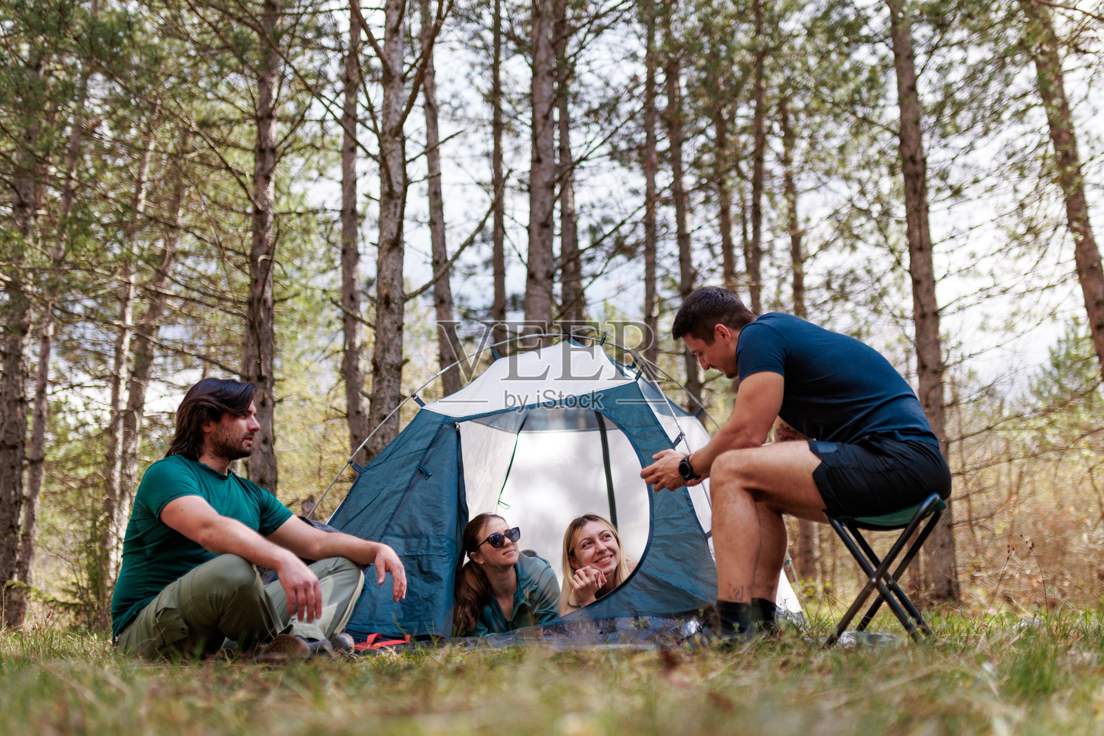 朋友们在阳光明媚的一天,在树林里享受露营之旅,围着帐篷分享故事,充满了欢声笑语和友谊。照片摄影图片