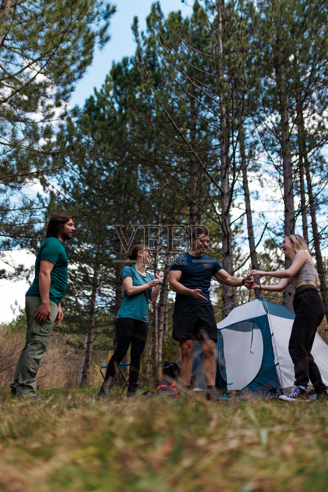 朋友们在森林里一起露营,搭帐篷,在阳光明媚的天空下分享欢笑,周围环绕着高大的树木。照片摄影图片
