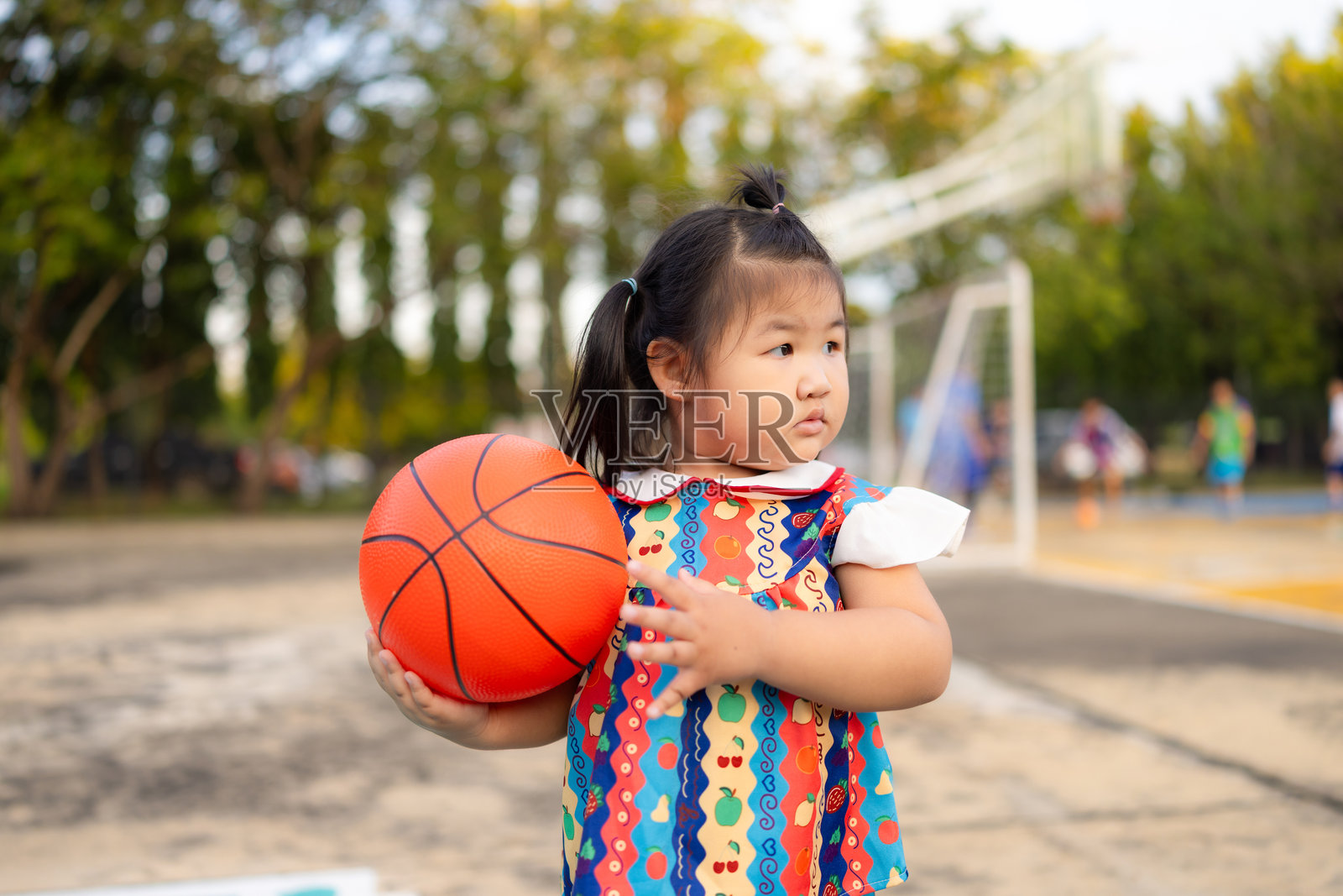 一个可爱的亚洲小女孩在球场上拿着篮球,一个穿着运动服的女孩在玩篮球比赛。照片摄影图片
