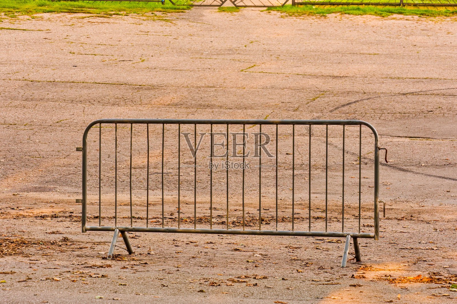 金属人群控制栅栏矗立在空旷的沥青地面上,地面散落着干枯的树叶。象征限制、安全、公共活动组织和城市基础设施。照片摄影图片