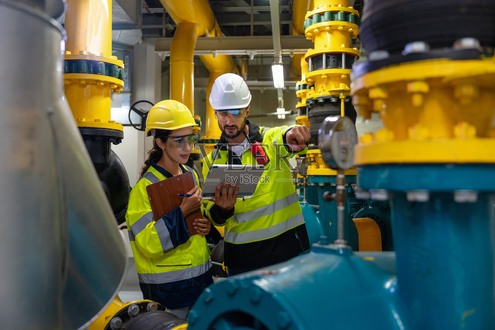 两位戴着安全帽的拉丁美洲工程师正在检查制冷系统,确保现代化工厂高效的制冷和供暖。照片摄影图片