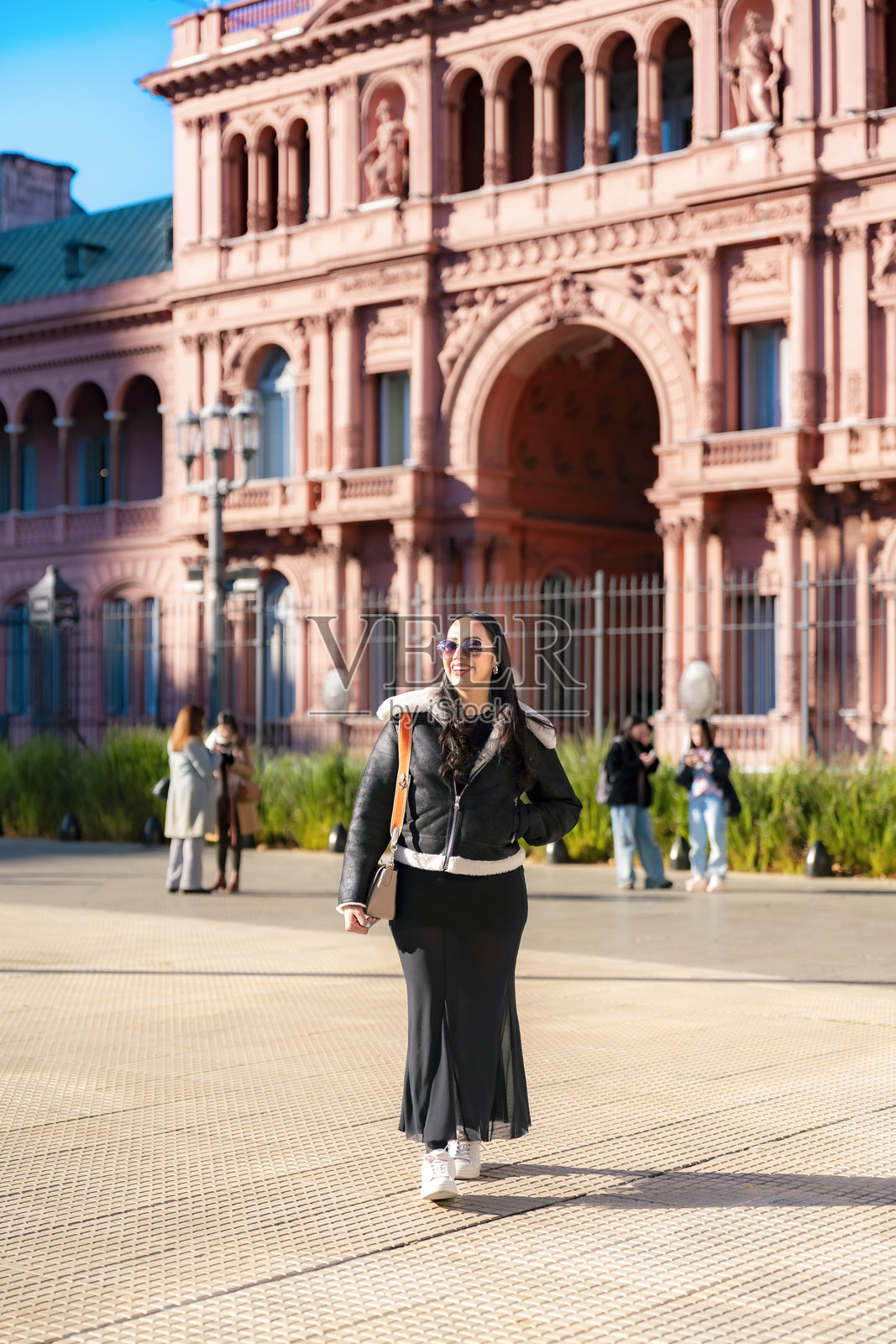 一位年轻的拉丁裔女士身穿黑色连衣裙和羊羔毛夹克,自信地在阿根廷布宜诺斯艾利斯玫瑰宫前摆姿势照片摄影图片