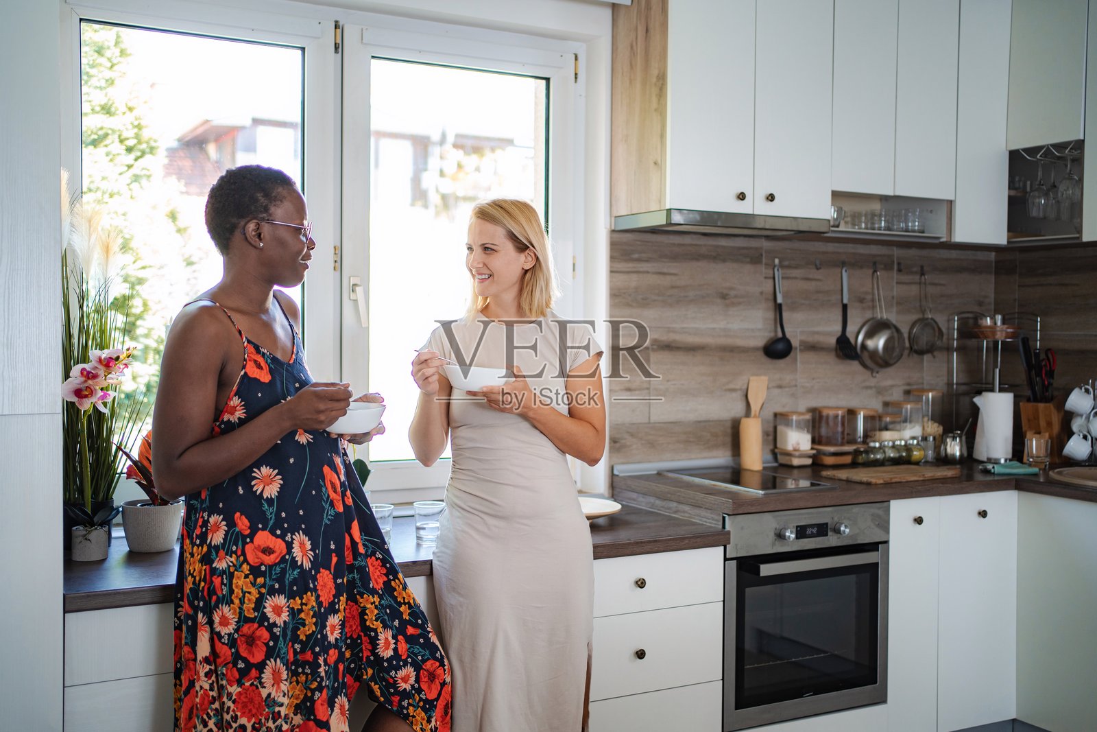 两位女士微笑着在现代厨房享用早餐并交谈照片摄影图片