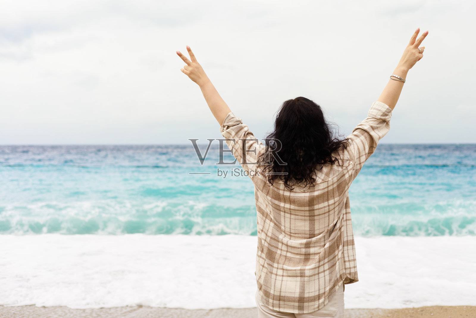 女子在海边举起双手比出胜利手势,享受着自由与快乐照片摄影图片