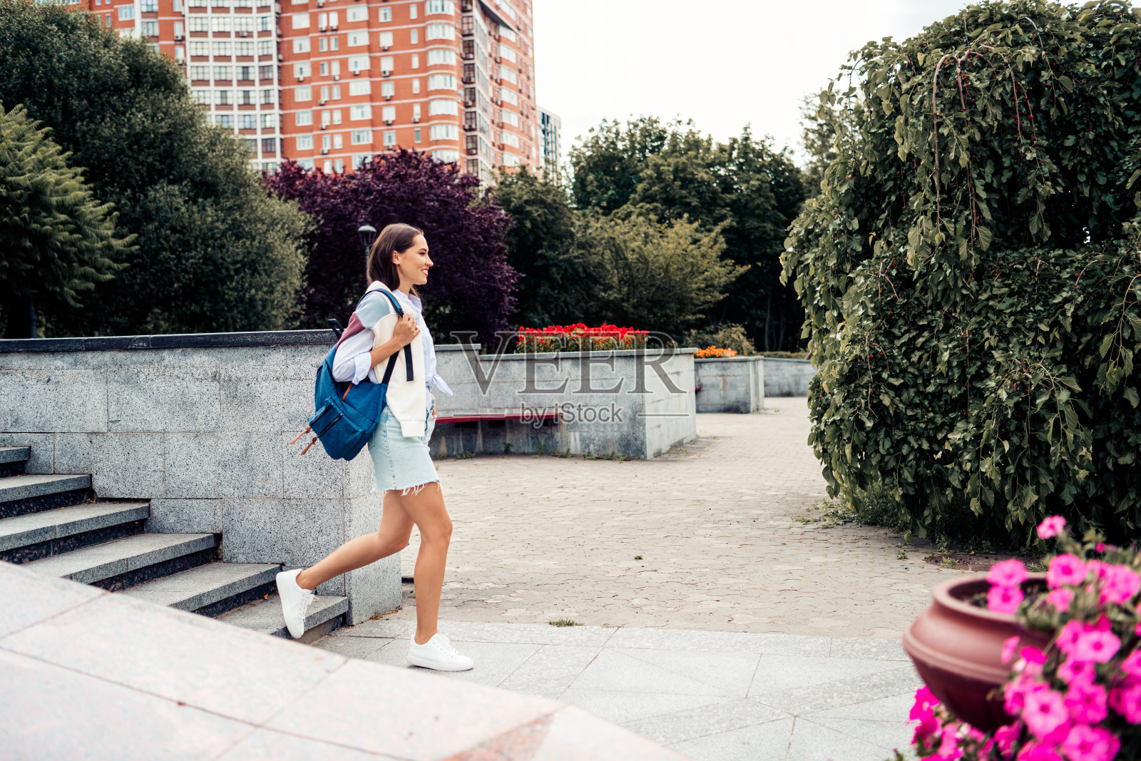 一位迷人的女士在休闲的一天里,背着背包走在城市公园里,展现出时尚休闲的户外风格照片摄影图片