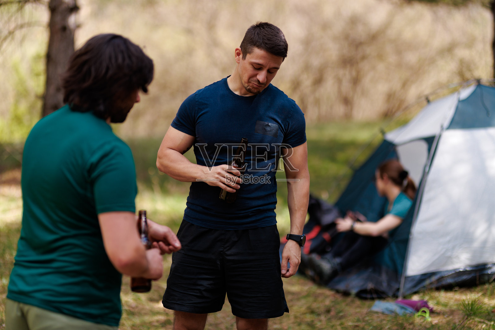 朋友们在阳光明媚的下午,在树林里的营地旁,在帐篷旁分享饮品,欢声笑语,享受着大自然的野营之旅。照片摄影图片