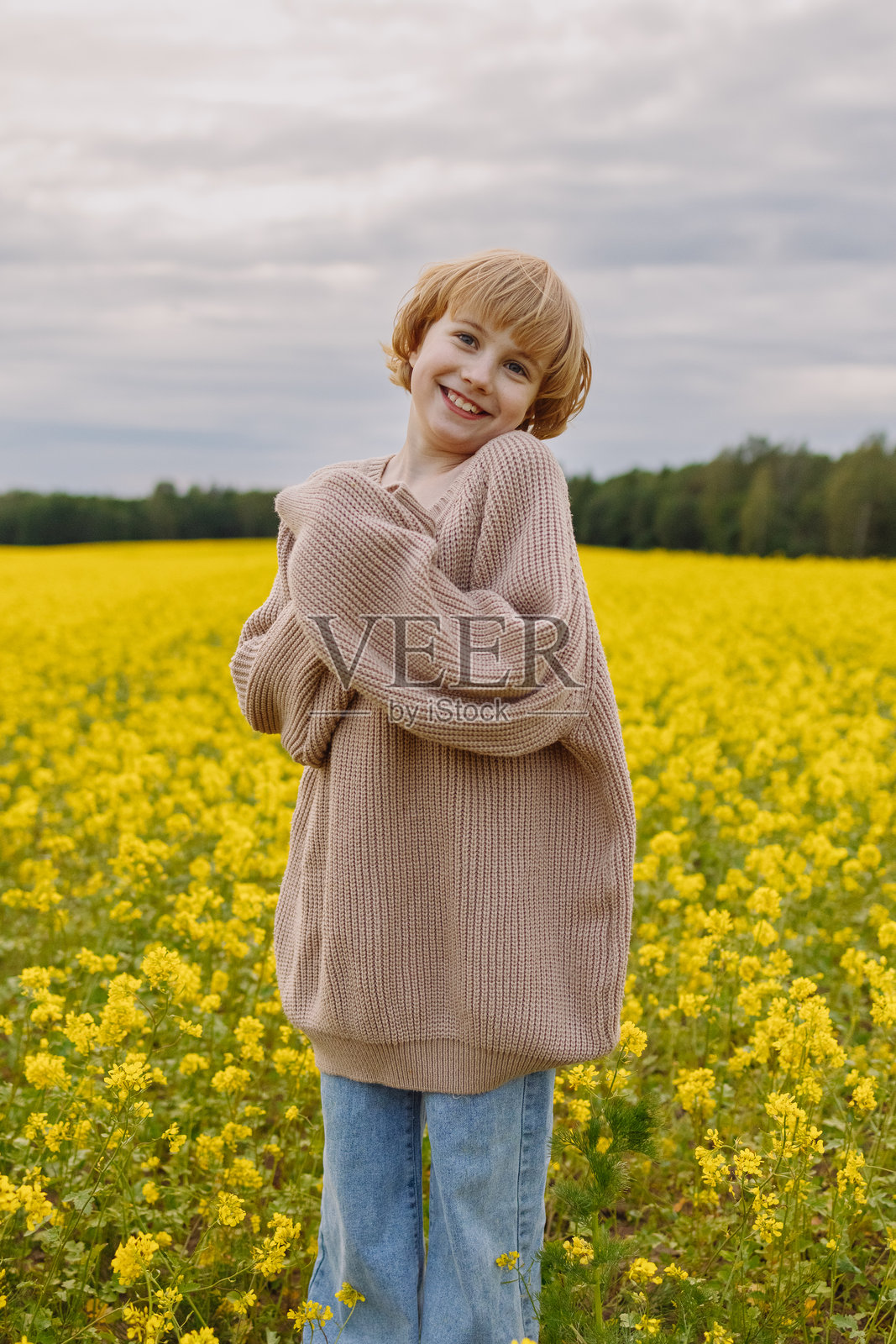 穿着米色毛衣的快乐女孩站在黄色油菜花田里看向镜头照片摄影图片