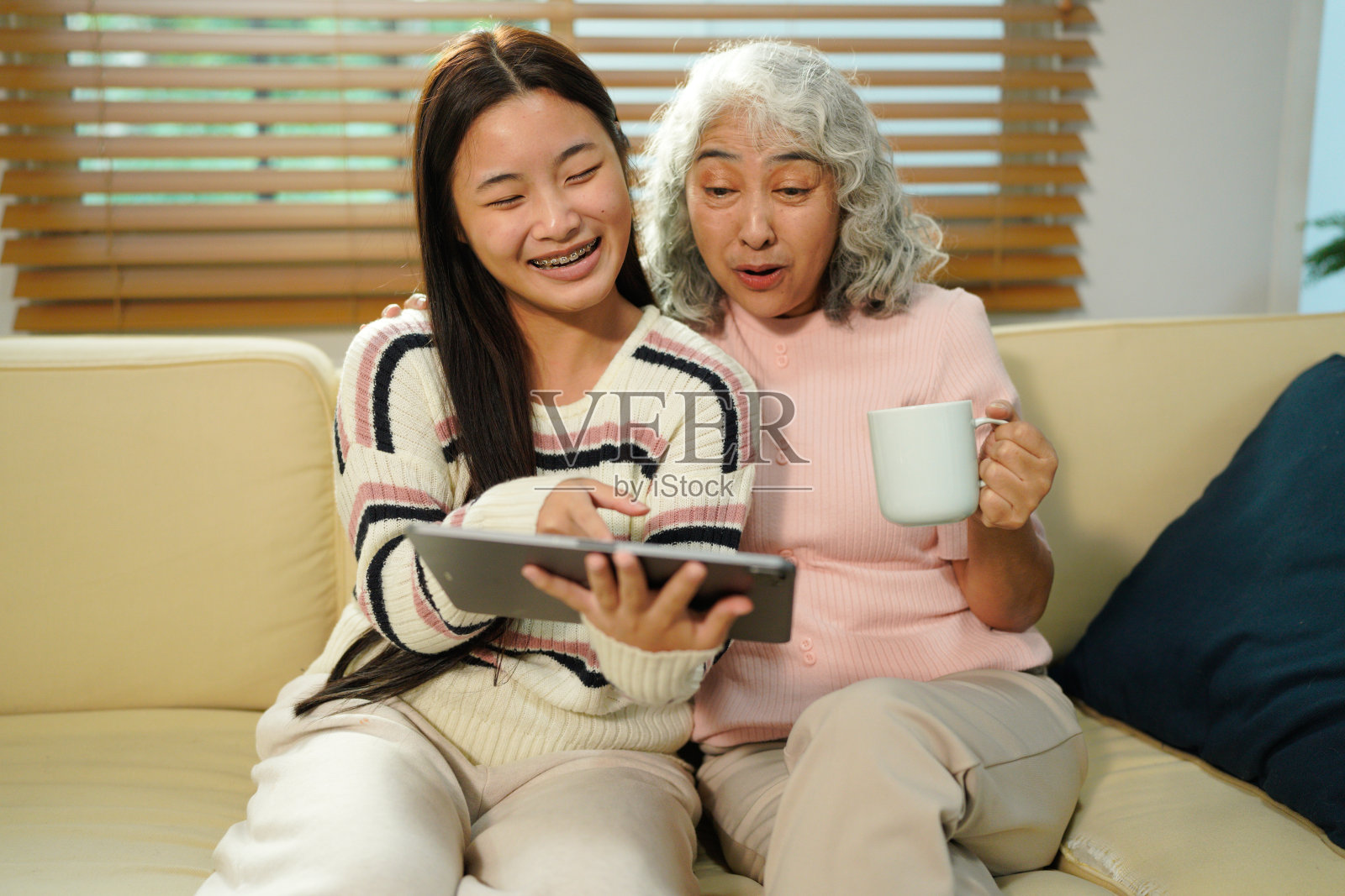 祖孙俩坐在沙发上,笑容满面地一起使用平板电脑。照片摄影图片