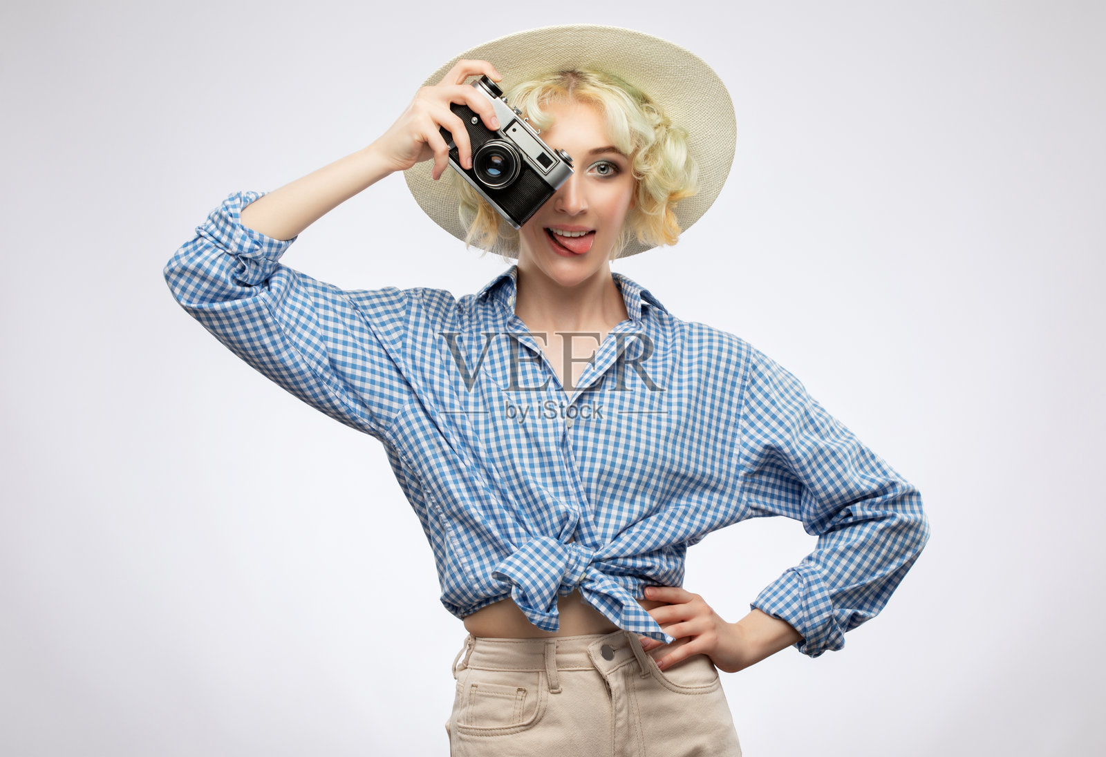 一位身穿蓝色格子衬衫、头戴草帽的漂亮迷人女摄影师,手持复古相机。旅游与旅行概念。照片摄影图片