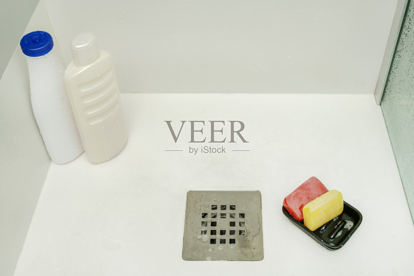 淋浴房,配有玻璃隔断和不锈钢排水口,摆放着甘油皂和洗发水瓶,瓶身上带有水珠。照片摄影图片