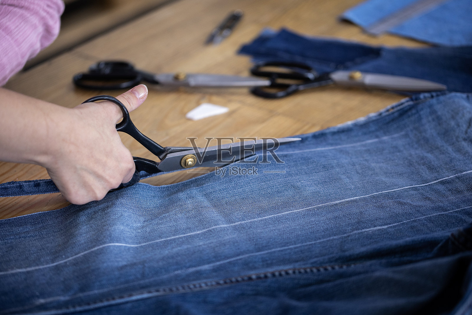 一位设计师用裁缝剪刀剪裁旧牛仔裤以制作新服装。这是一个关于升级回收、回收利用以及用牛仔布料创造可持续、环保时尚的概念。照片摄影图片