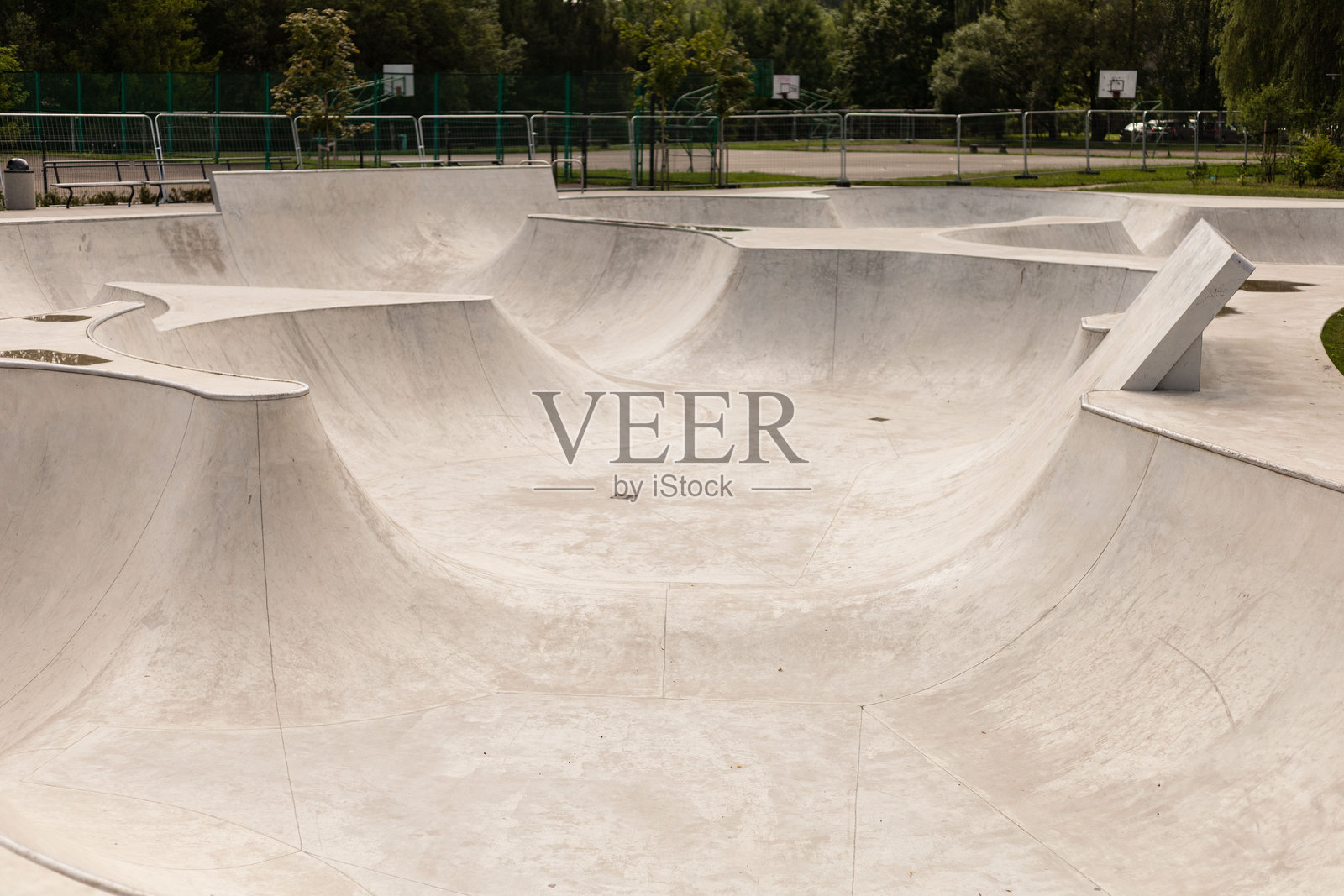 宽敞的滑板公园拥有光滑的混凝土曲面和坡道,吸引着滑板爱好者在此练习技巧,享受周围充满活力的绿色环境。这是一个阳光明媚的日子,非常适合户外娱乐。照片摄影图片