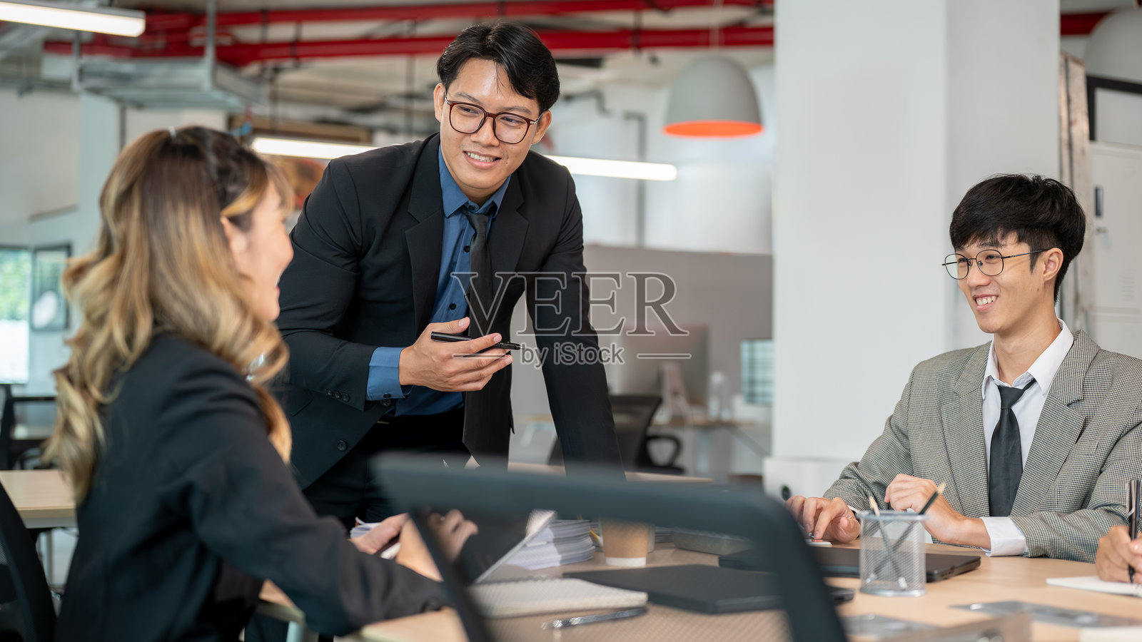 商人正在办公室的会议上,在木桌旁与女同事交谈,手中拿着一支笔。照片摄影图片