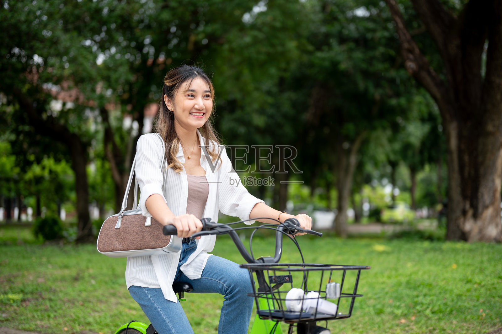 一位漂亮的亚洲女性在自然公园里骑着绿色自行车,面带微笑,享受着悠闲的时光。照片摄影图片