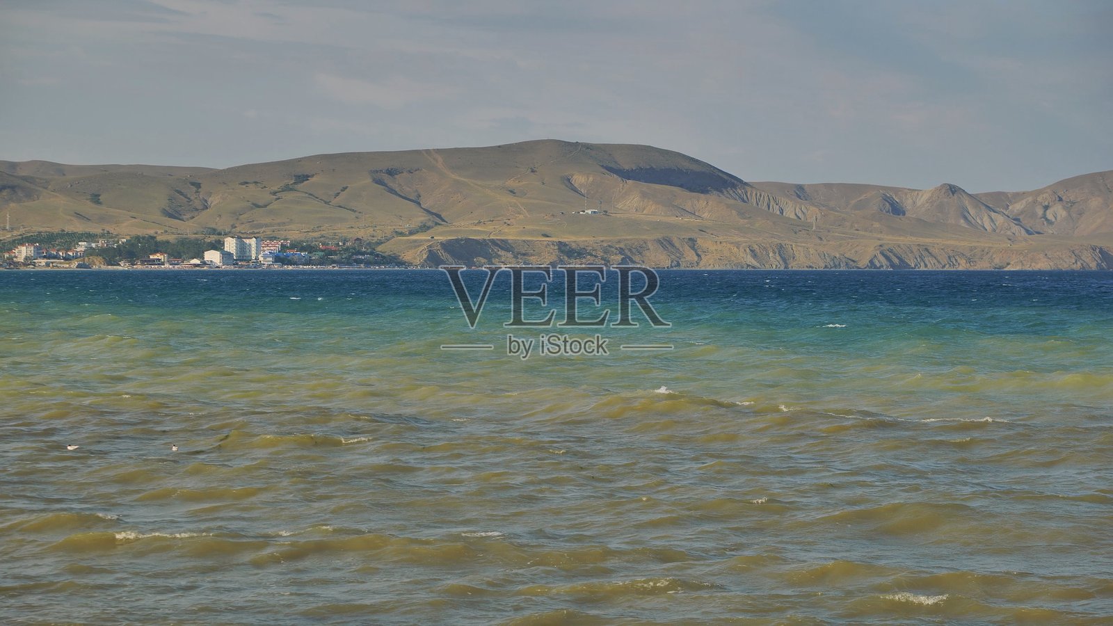 风帆冲浪者在阳光明媚的日子里享受黑海的波浪,背景中可以看到克里米亚海岸线。照片摄影图片