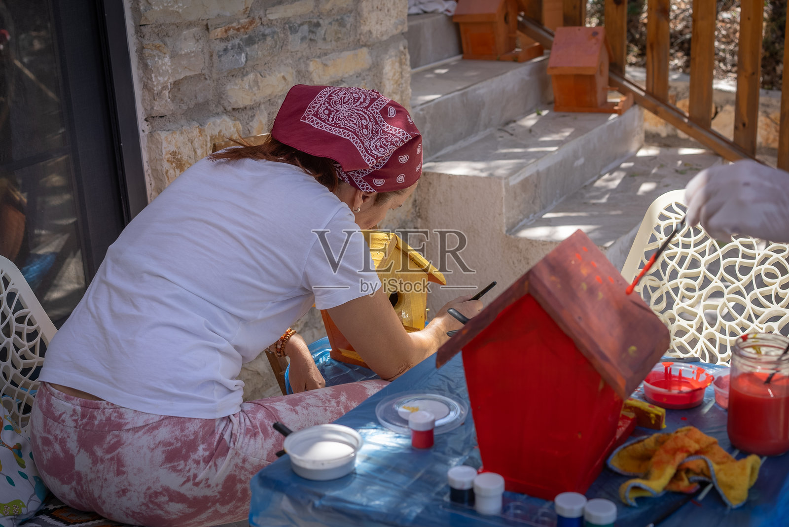 一位成熟的女性在质朴的石头房子的门廊上绘制鸟舍照片摄影图片