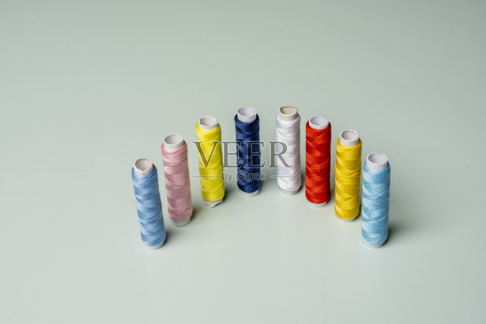 一排排彩色线轴垂直排列在一个光滑的粉蓝色表面上照片摄影图片