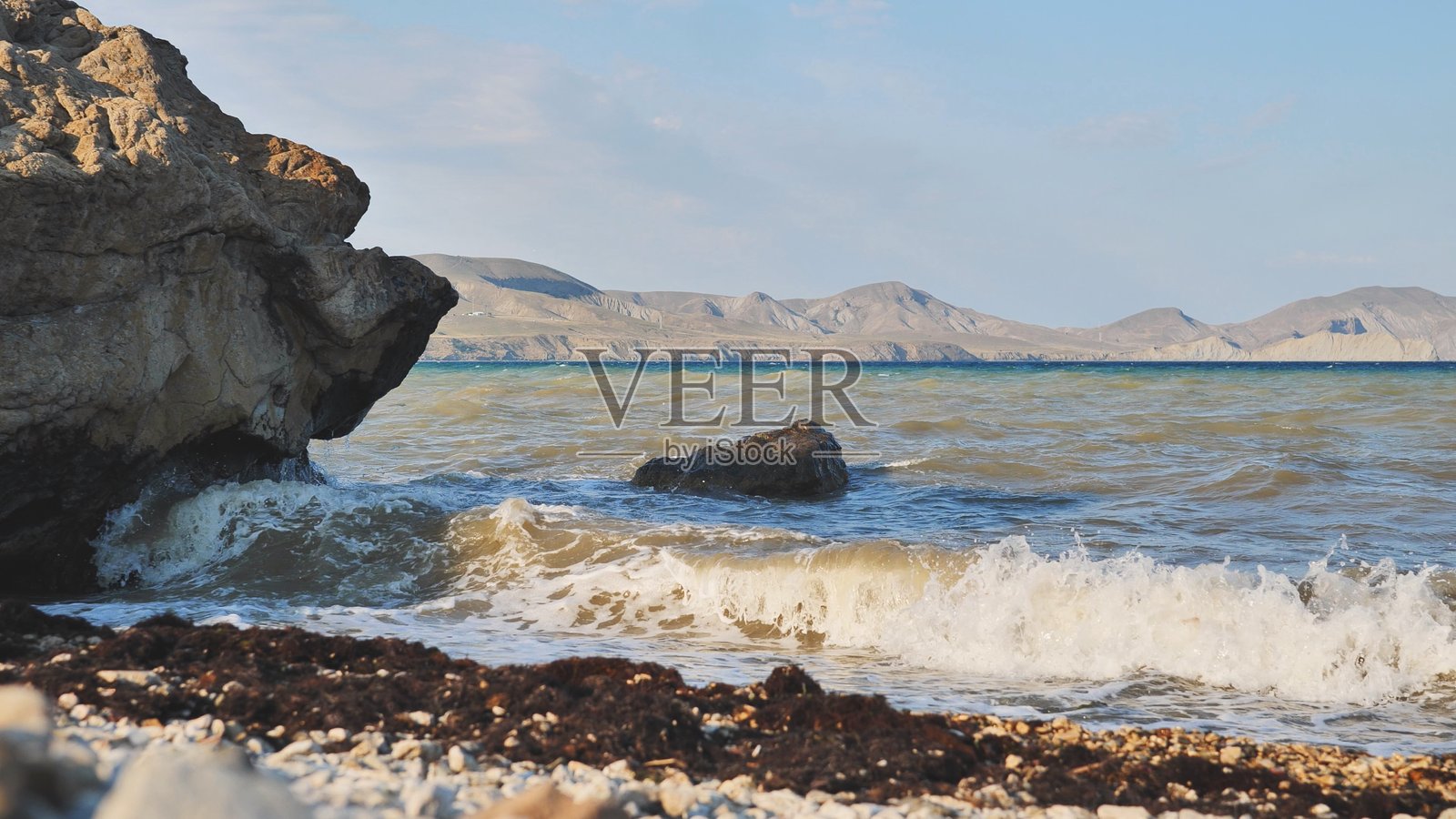 海浪拍打着克里米亚多岩石的海滩,背景是群山。照片摄影图片