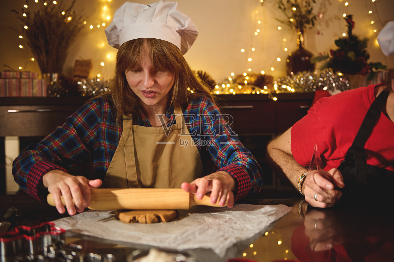 厨师戴着白色厨师帽,在节日厨房里用擀面杖擀面团,节日烘焙场景,暖色灯光照片摄影图片