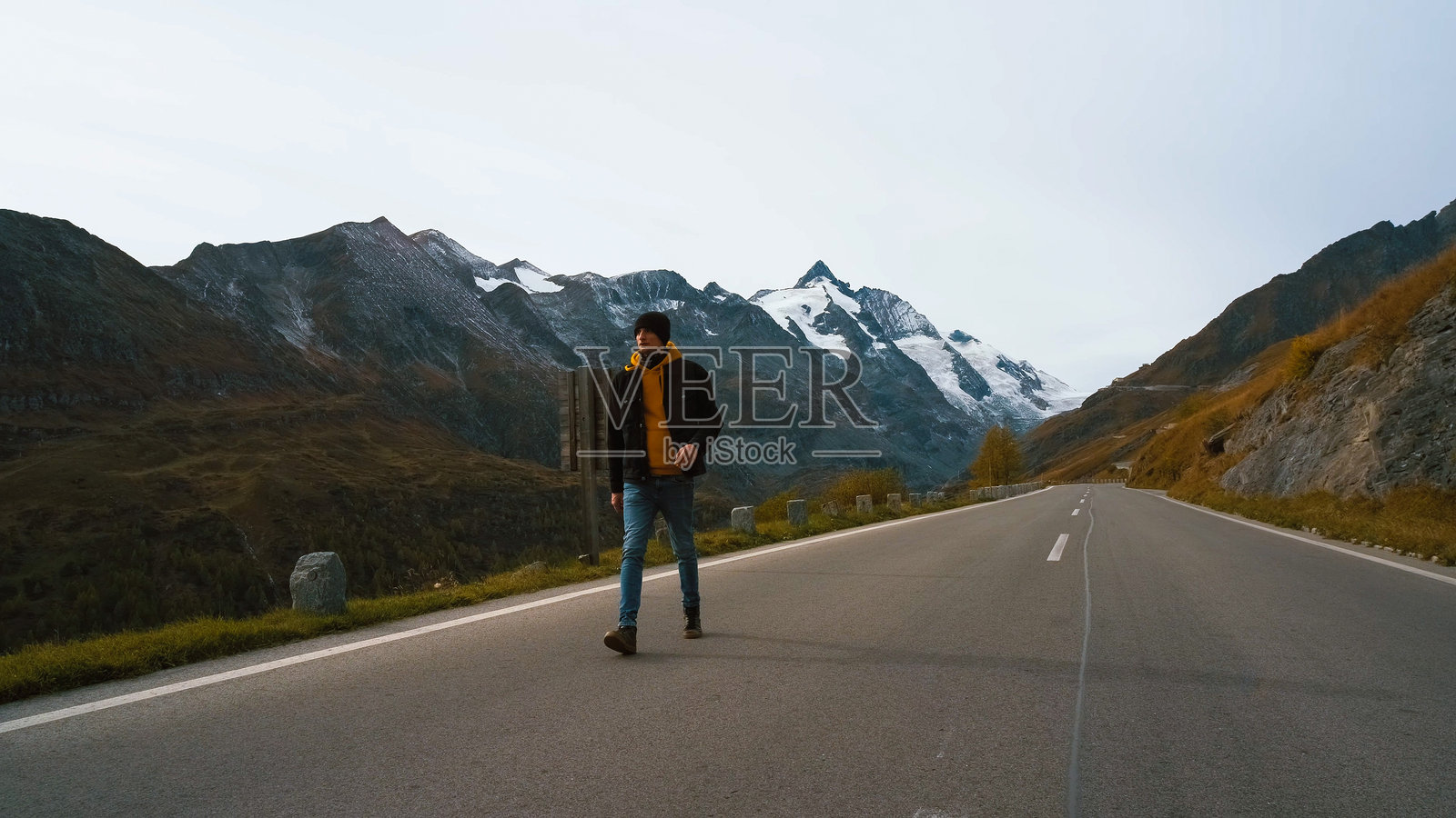 晴天,男子在山路上行走,背景是白雪皑皑的山峰照片摄影图片