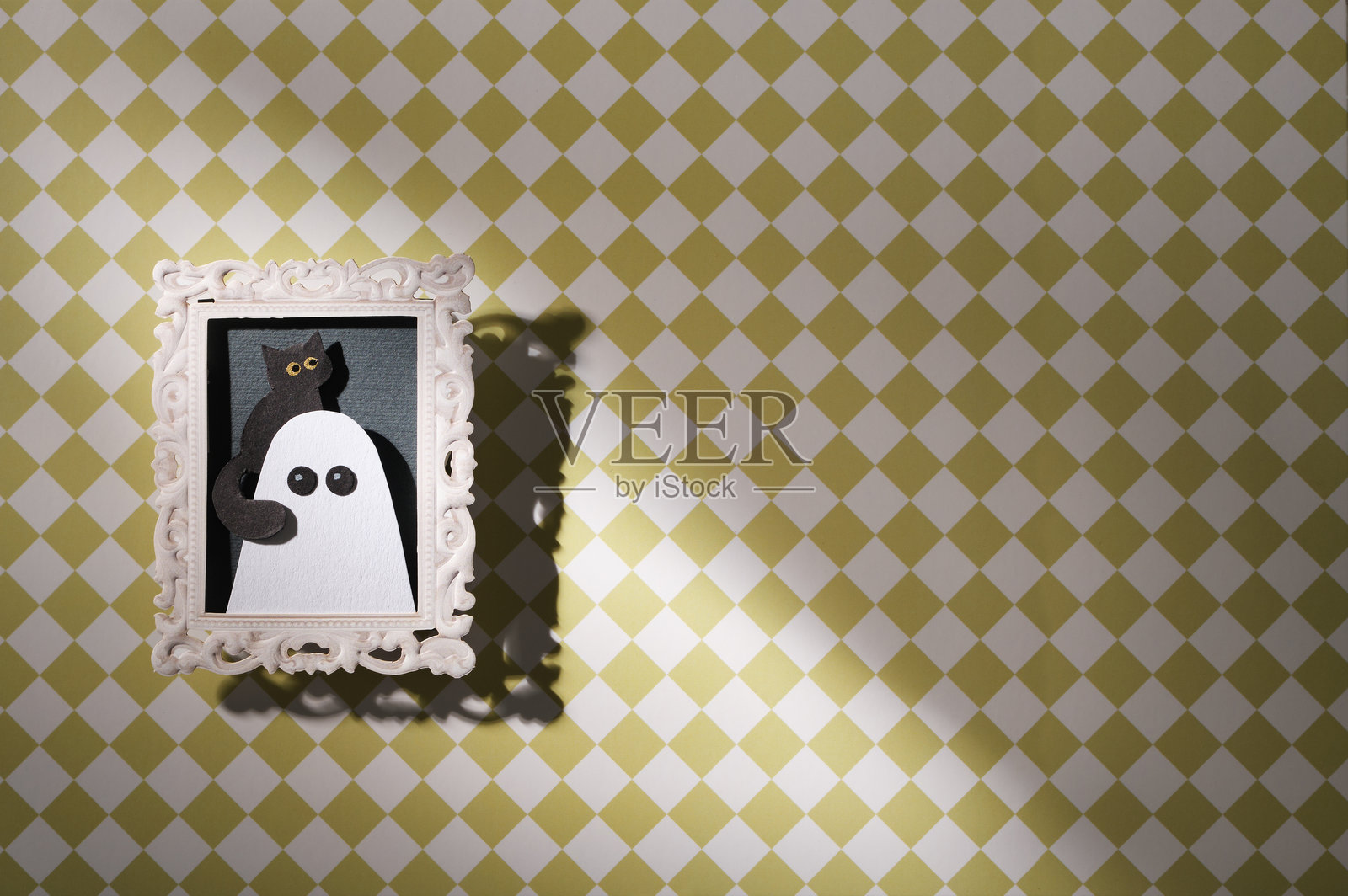 手工万圣节工艺品。一个鬼魂带着他的宠物黑猫挂在格子墙纸的墙上,留有空白空间。照片摄影图片