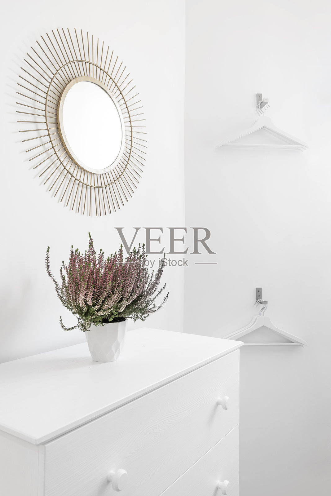 度假出租屋卧室一角,配有白色抽屉柜、配套衣架和金属框镜子照片摄影图片