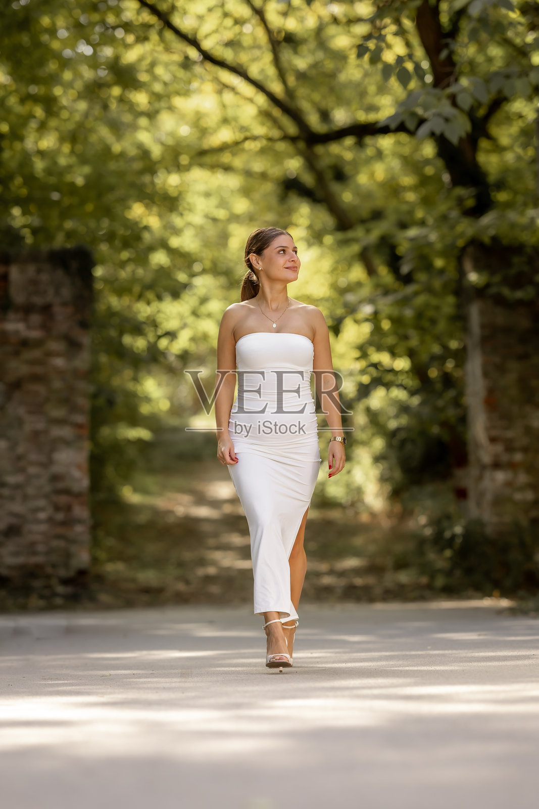 身穿优雅连衣裙的女子在公园里漫步,面带微笑照片摄影图片