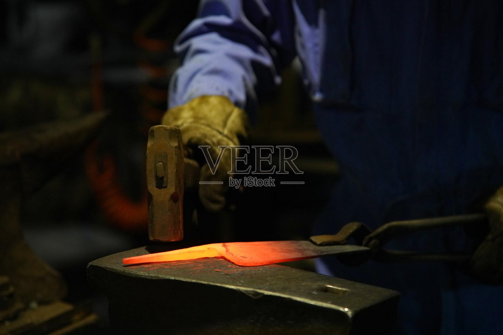 一位工匠正在将加热的材料锻造成形照片摄影图片