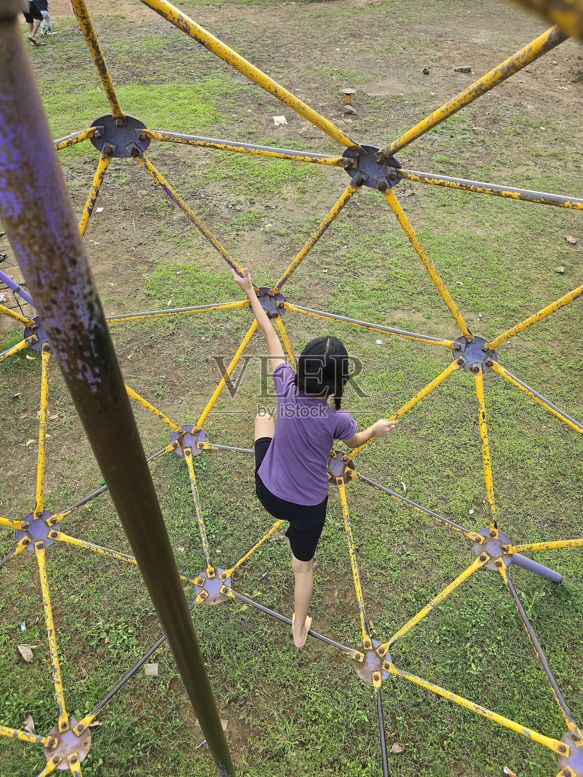 小女孩专注而努力地攀爬着游乐场设施,抓着金属栏杆,营造出愉快的户外氛围照片摄影图片