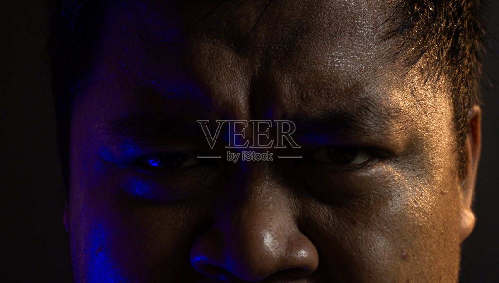 愤怒的亚洲男子特写肖像,表情丰富,冷暖色调混合打光,深色背景凸显情感与力量。照片摄影图片