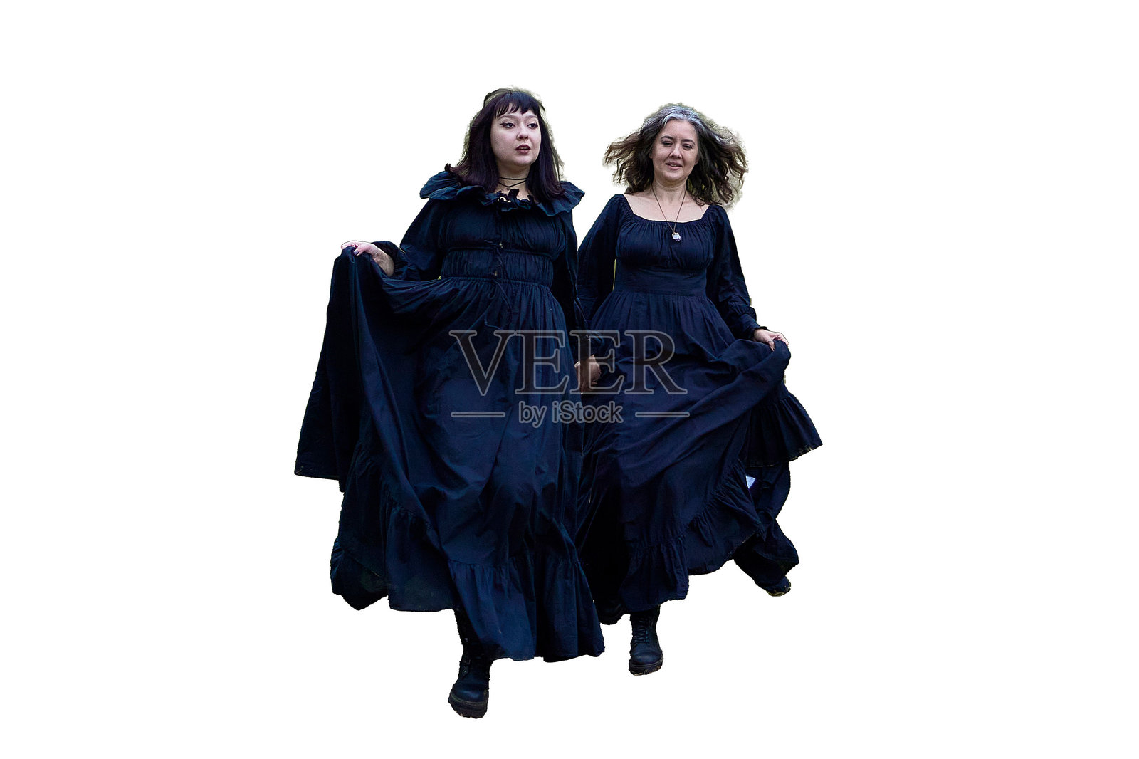 两位身着爱德华时代长款黑裙的女性,正在一棵雄伟的橡树旁的山坡上,进行一场历史重现,扮演着万圣节的恋人共舞。照片摄影图片