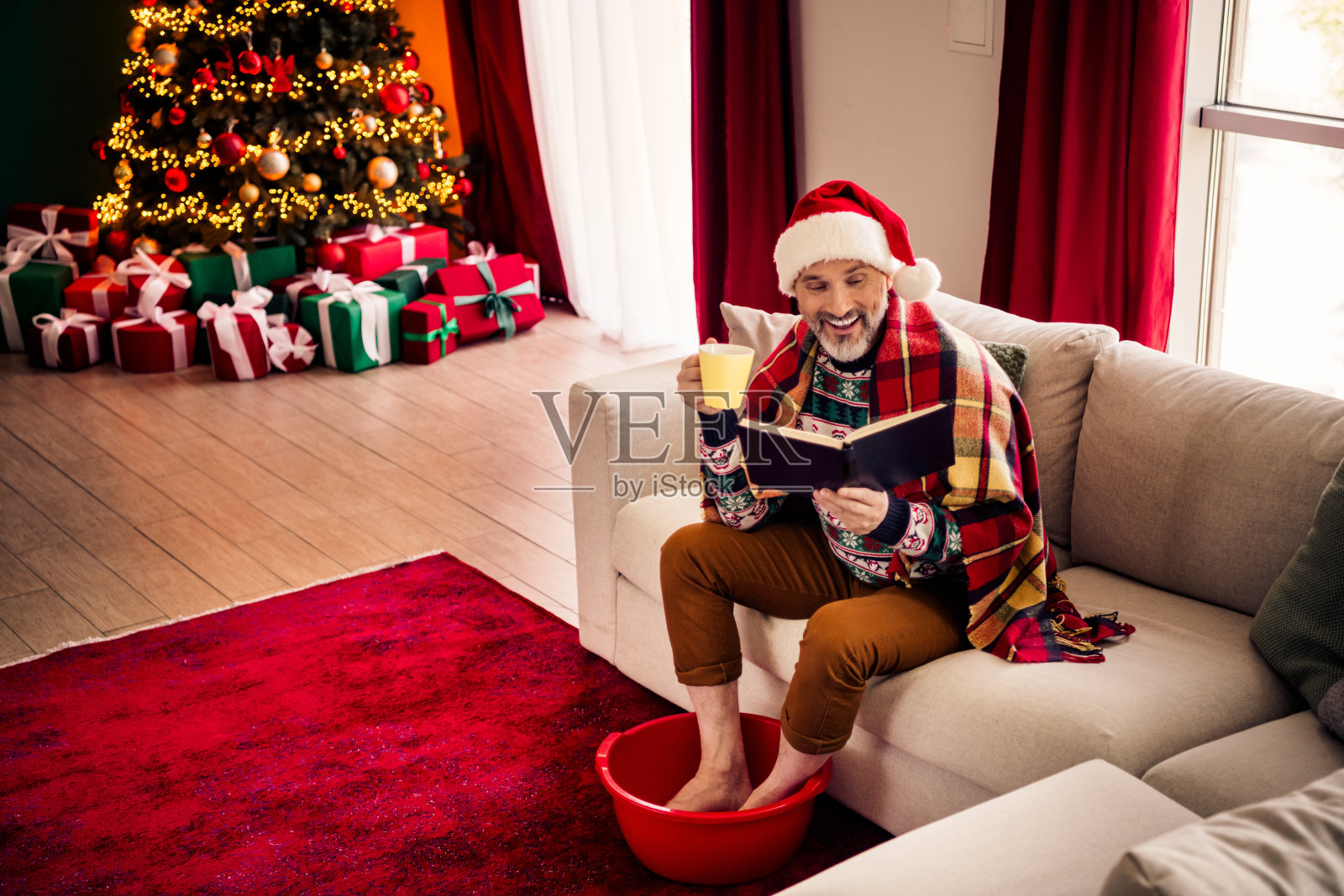 一位老人正在享受一个轻松的圣诞早晨,周围有礼物、舒适的装饰和节日带来的欢乐,营造出温馨的节日氛围。照片摄影图片