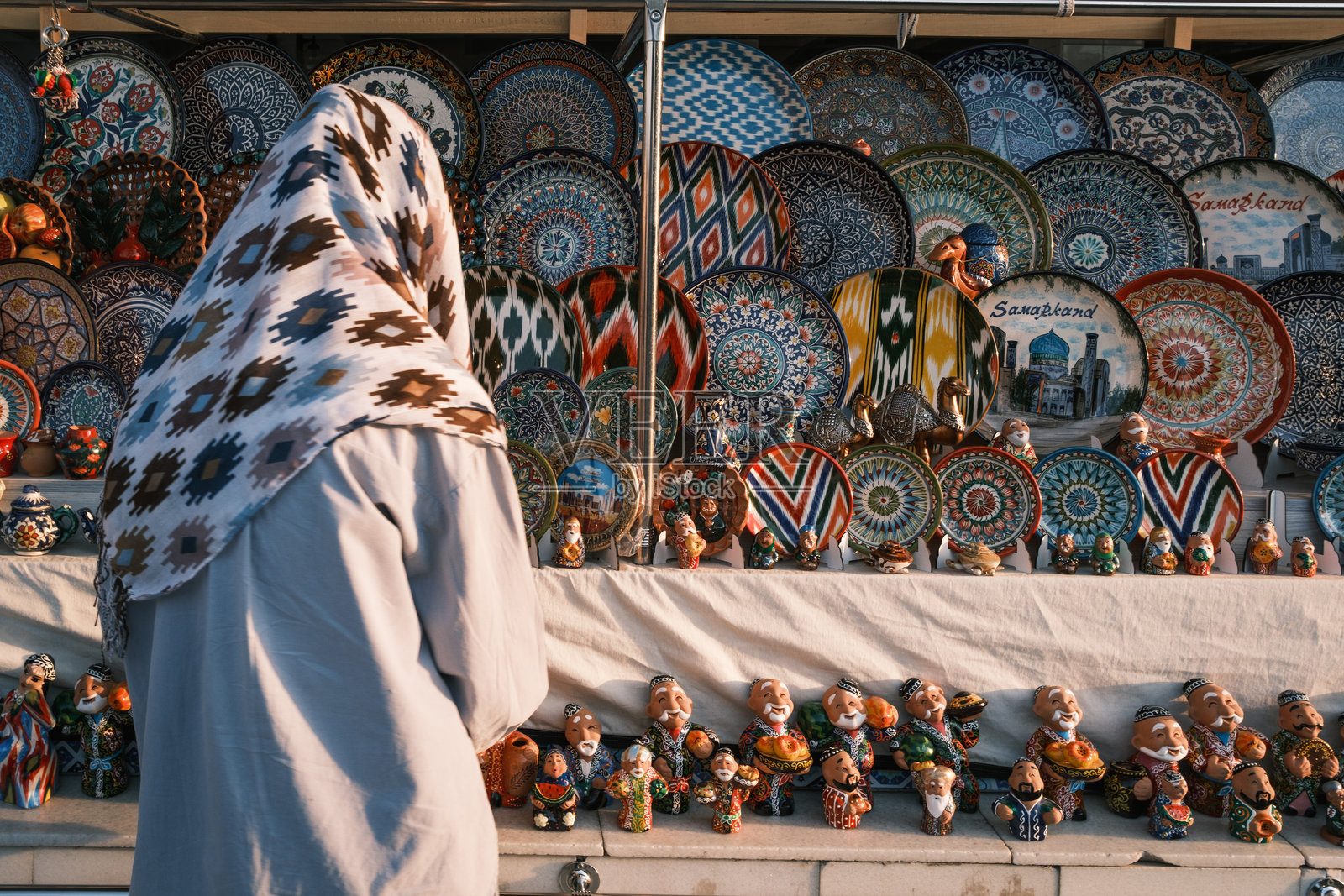 乌兹别克斯坦撒马尔罕热闹的集市上,当地商贩被精美的陶瓷盘和传统的乌兹别克手工艺品环绕。照片摄影图片