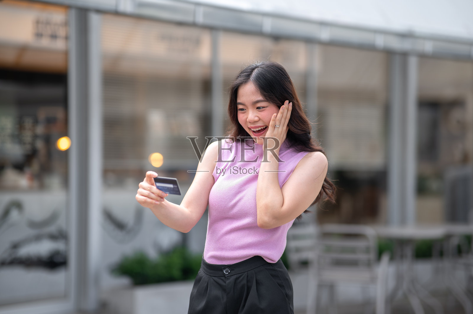 一名年轻亚洲女子站在咖啡馆前或走过时,惊讶地看着信用卡照片摄影图片