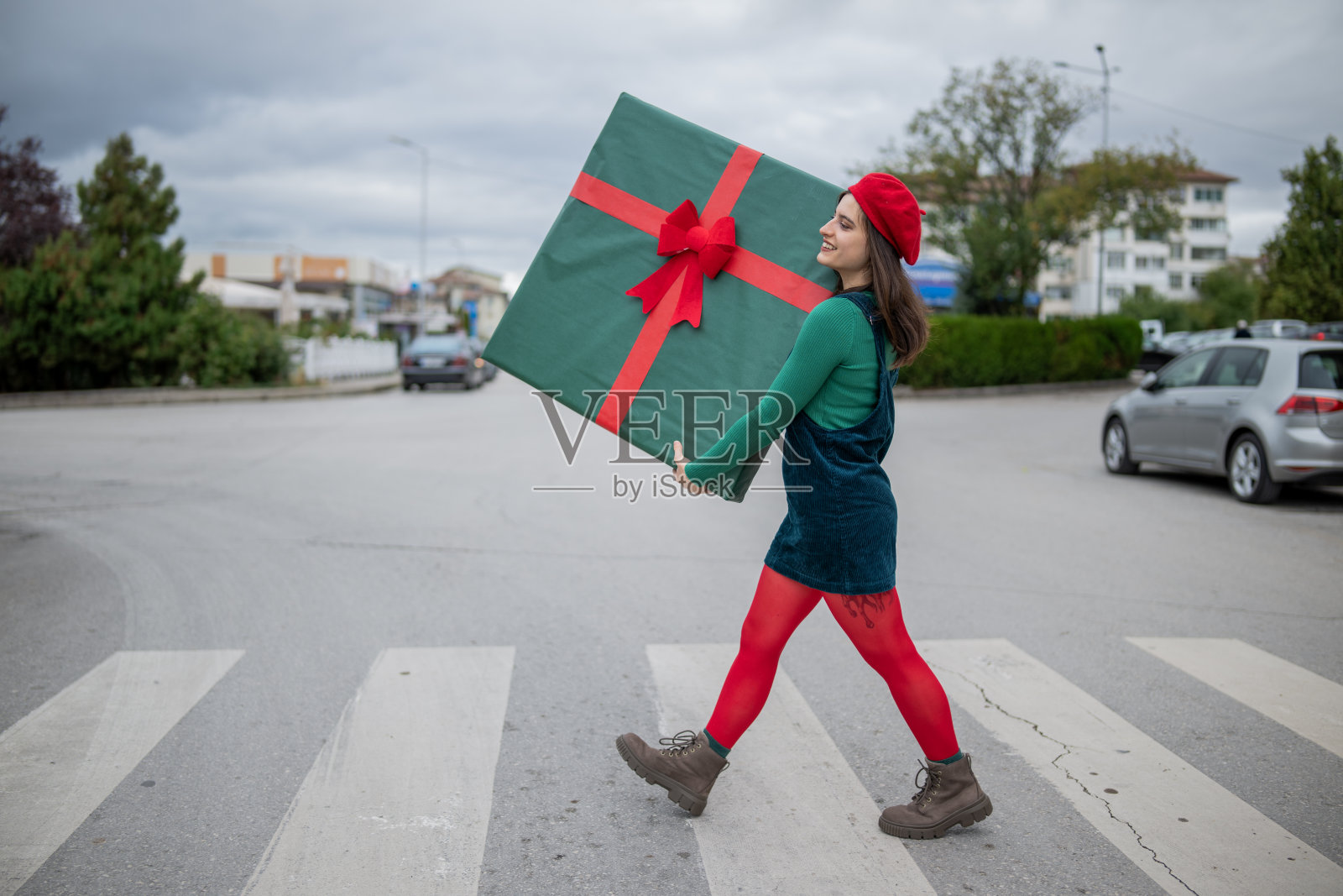 年轻女子在街上背着巨大的圣诞礼物过马路。照片摄影图片