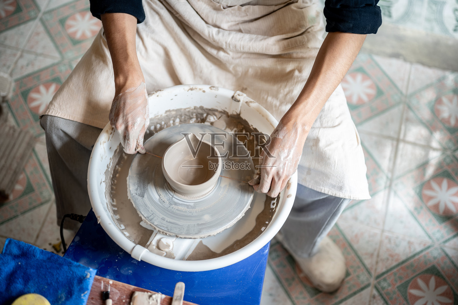 陶艺师在教室或工作室的拉坯机上,使用钢丝切割器处理正在制作的陶碗,用于泡茶。照片摄影图片