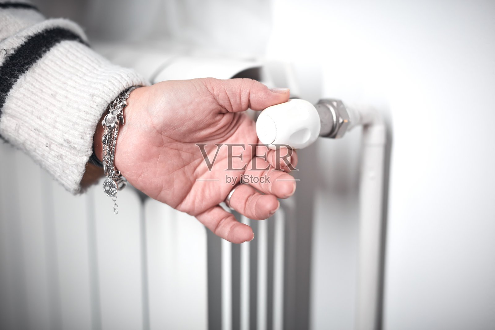 寒冷的冬日,女子正在转动暖气片阀门,能源和天然气危机,房间寒冷,供暖问题。照片摄影图片
