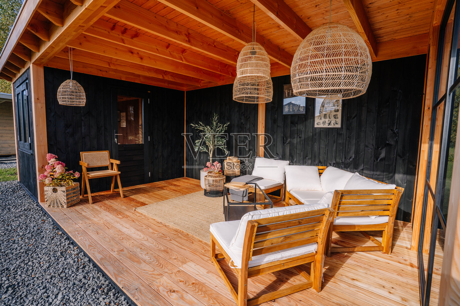 现代小屋风格的时尚户外休息区,配有木制家具、白色靠垫、柳条吊灯、黑色木质镶板和舒适的装饰。照片摄影图片