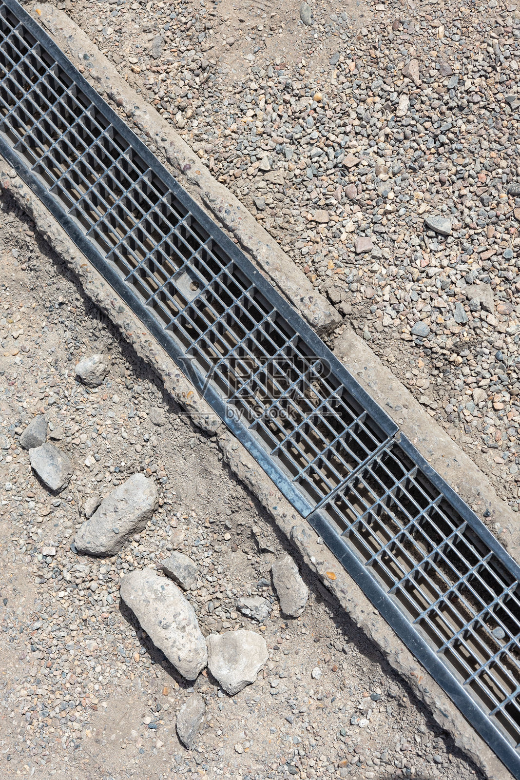 施工现场路边碎石地面上安装的金属排水篦,可实现排水并防止道路附近堆积杂物照片摄影图片