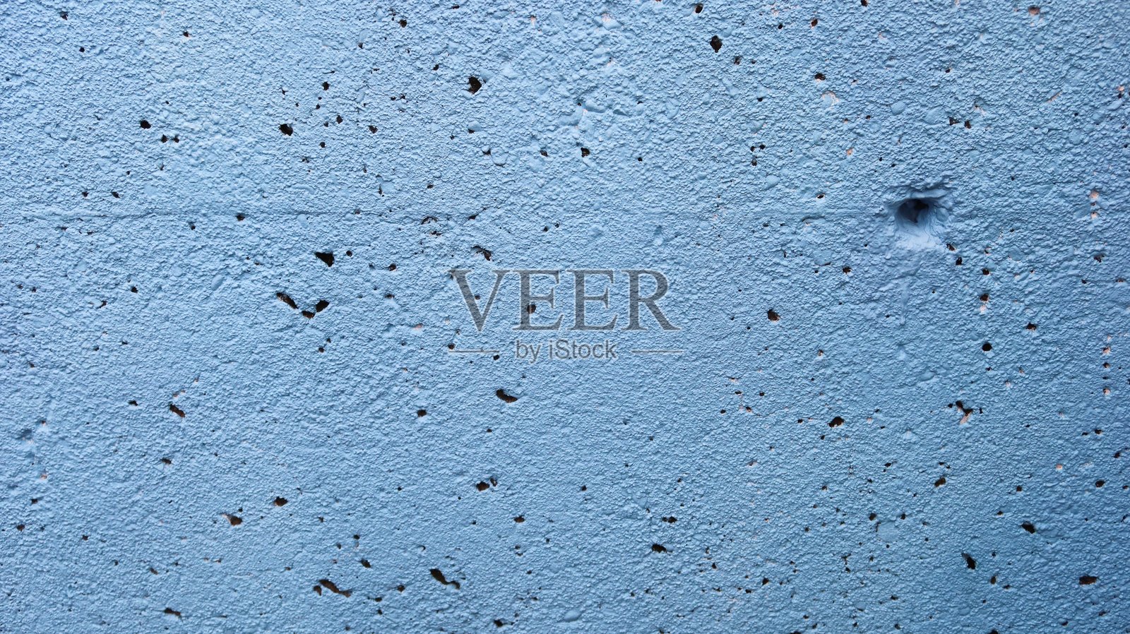 近距离拍摄的粗糙不平的墙壁,上面布满了鲜艳的蓝色涂料和许多孔洞照片摄影图片
