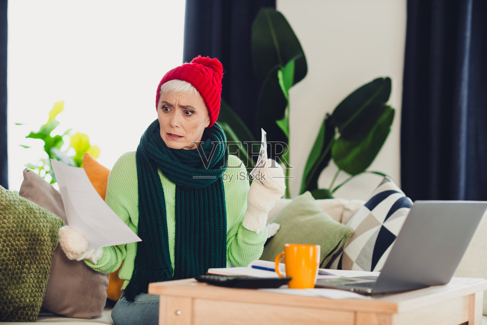 一位成熟的女性在舒适的客厅环境中,手持文件和笔记本电脑,正在室内查看水电费账单。照片摄影图片
