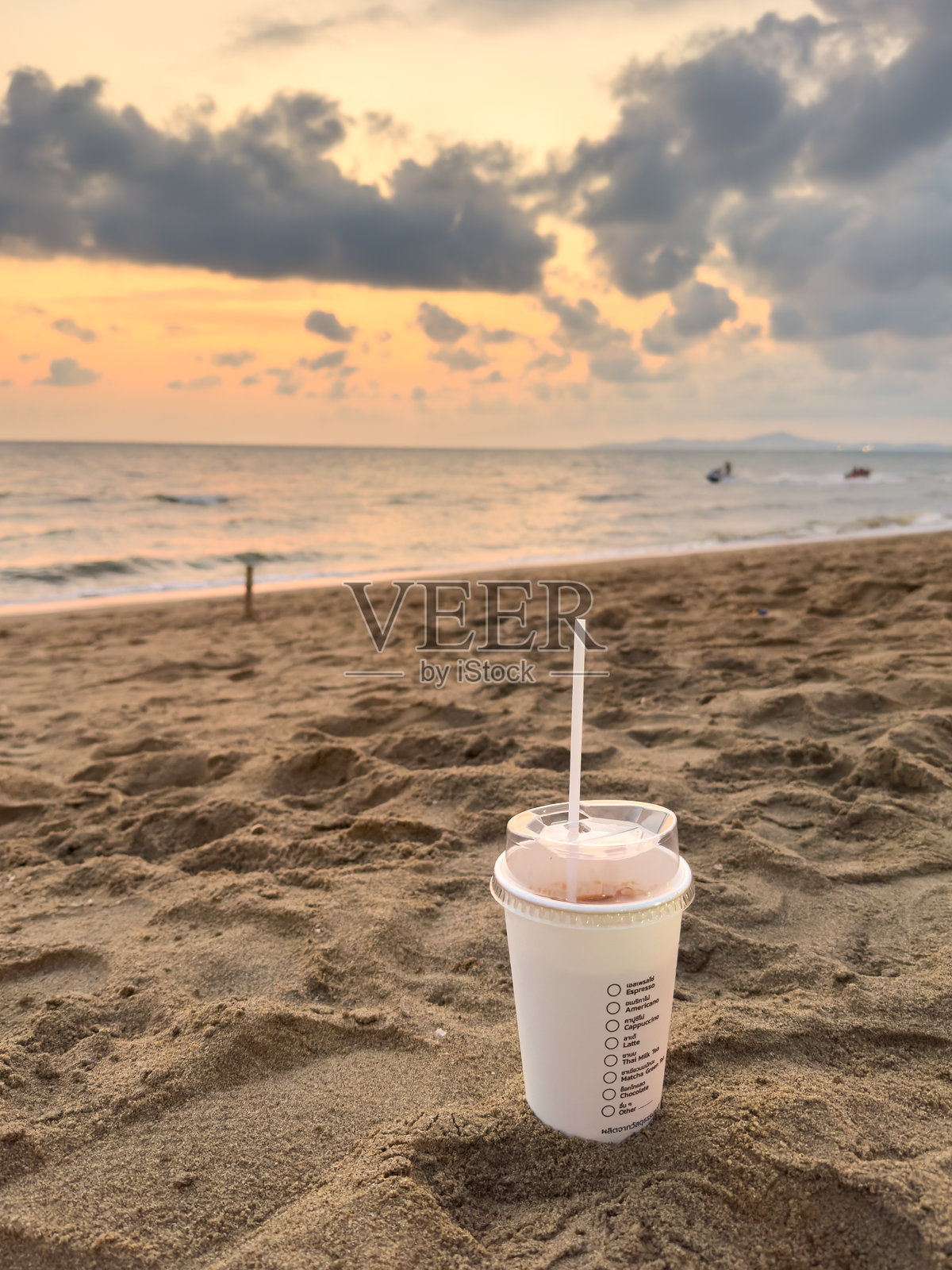 夕阳下的泰国芭堤雅沙滩上,放着一杯冰咖啡。温柔的海浪拍打着海岸,温暖的云彩天空下,营造出宁静的热带夜晚景象。照片摄影图片