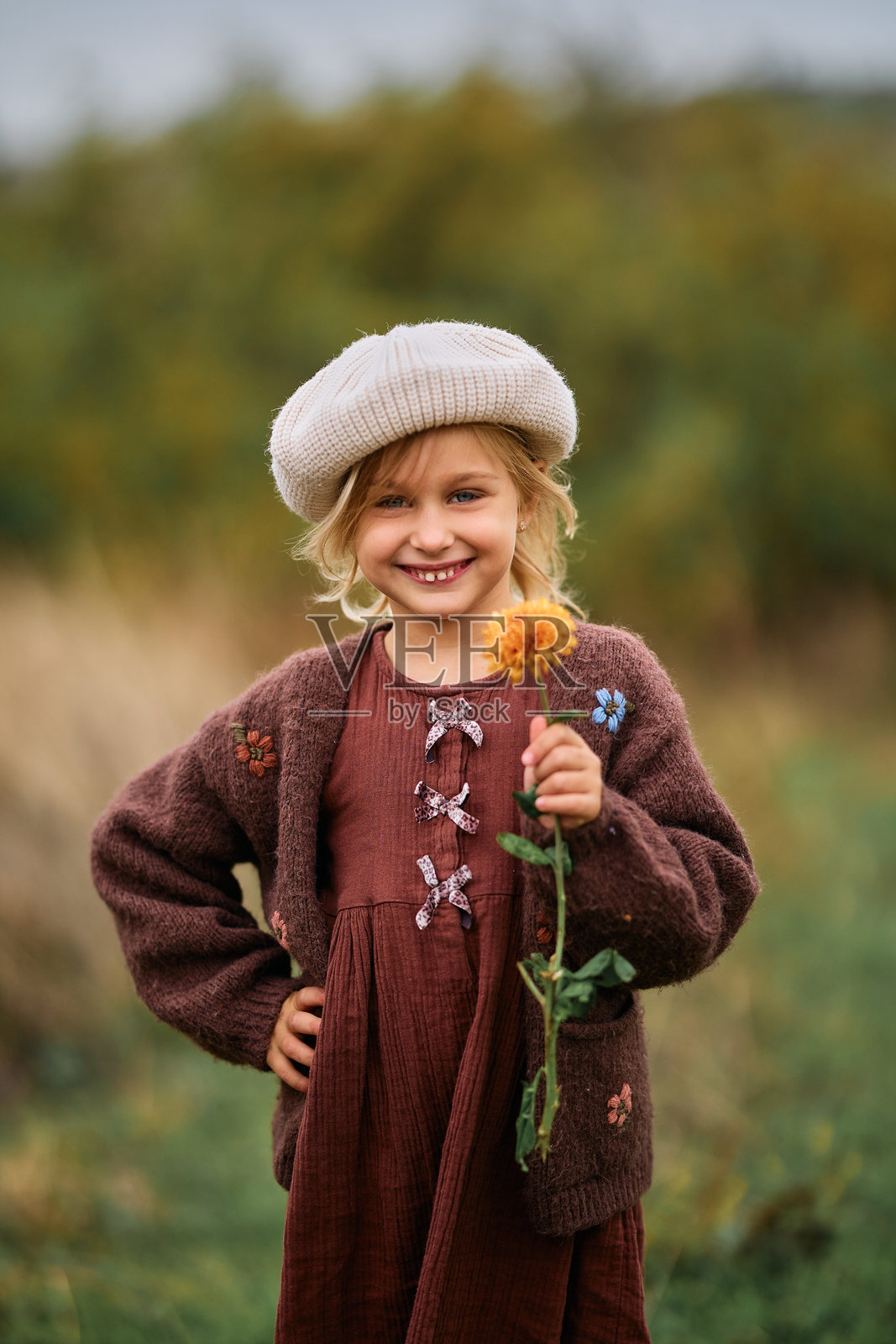 秋日田野里,一位年轻的女孩微笑着,手里拿着一朵花。照片摄影图片