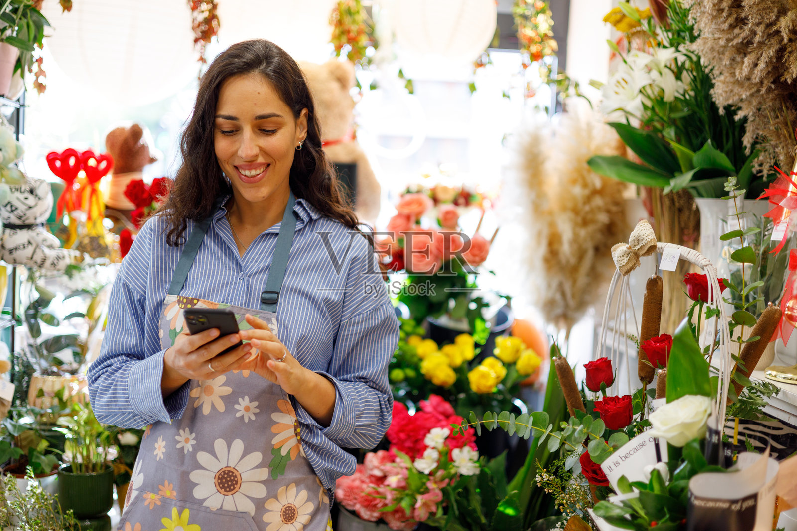 一位女花店老板正在使用智能手机管理线上订单,打理她的花店生意。照片摄影图片