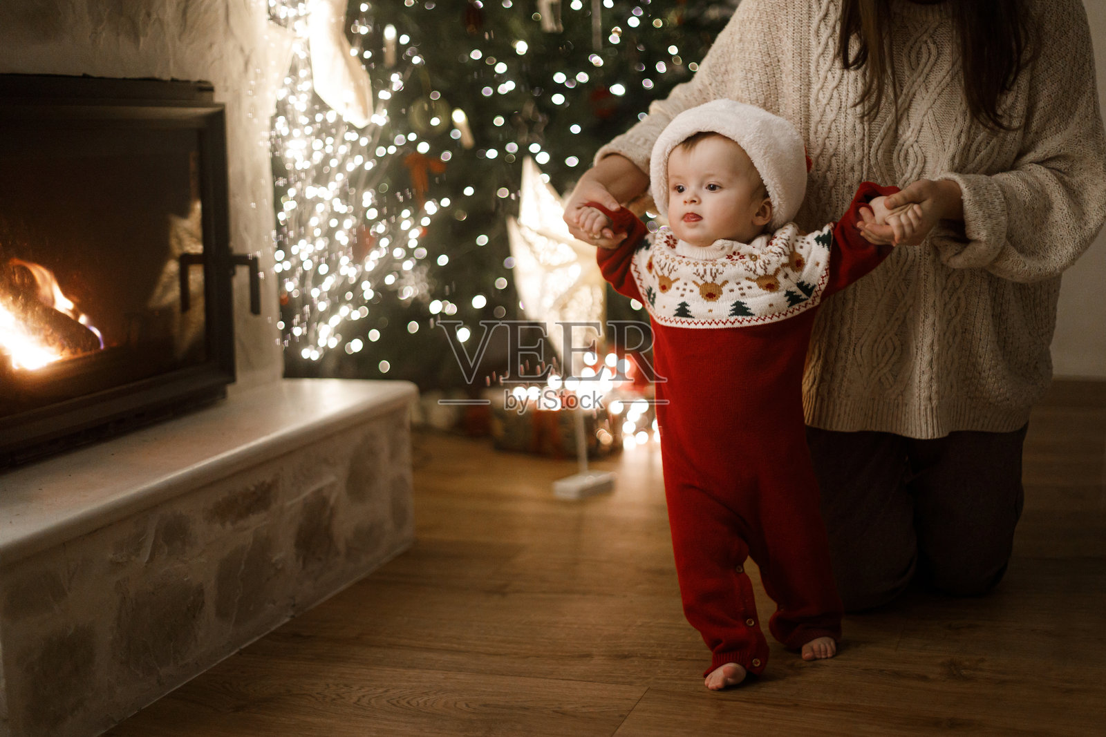 温馨的圣诞夜,一家人沉浸在魔法般的节日氛围中。圣诞快乐,节日吉祥!妈妈抱着可爱的宝宝,穿着节日毛衣,在装饰时尚的圣诞树旁散步,树下摆放着礼物和彩灯。照片摄影图片