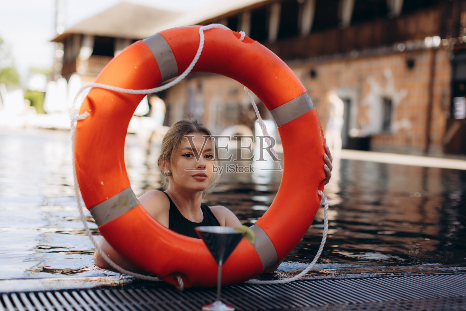女子在泳池中放松,身旁有救生圈和鸡尾酒照片摄影图片
