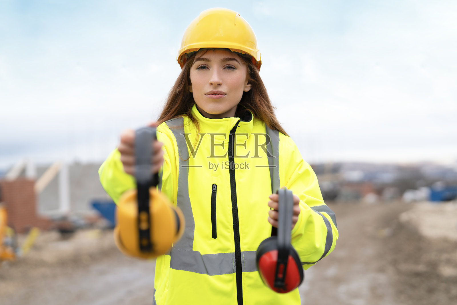 建筑工地标准安全防护用品的概念。一位女建筑工人展示耳罩。照片摄影图片