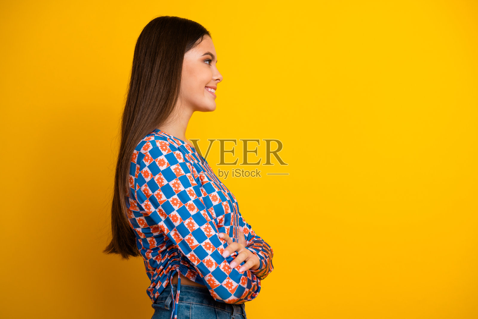 一位年轻拉丁女性的肖像,她有着棕色的长发,穿着蓝橙格纹上衣,站在明亮的黄色背景前照片摄影图片