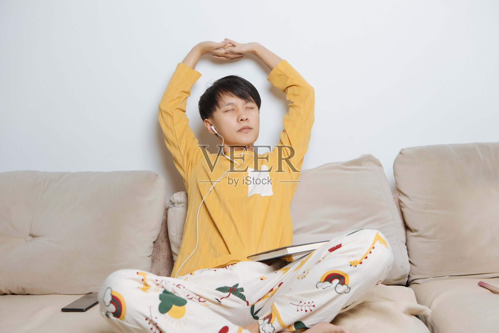 清晨,年轻的亚洲男子坐在舒适的家中沙发上,伸展着手臂和背部,享受着简单健康的生活方式、个人休闲和明亮现代客厅的室内健康。照片摄影图片